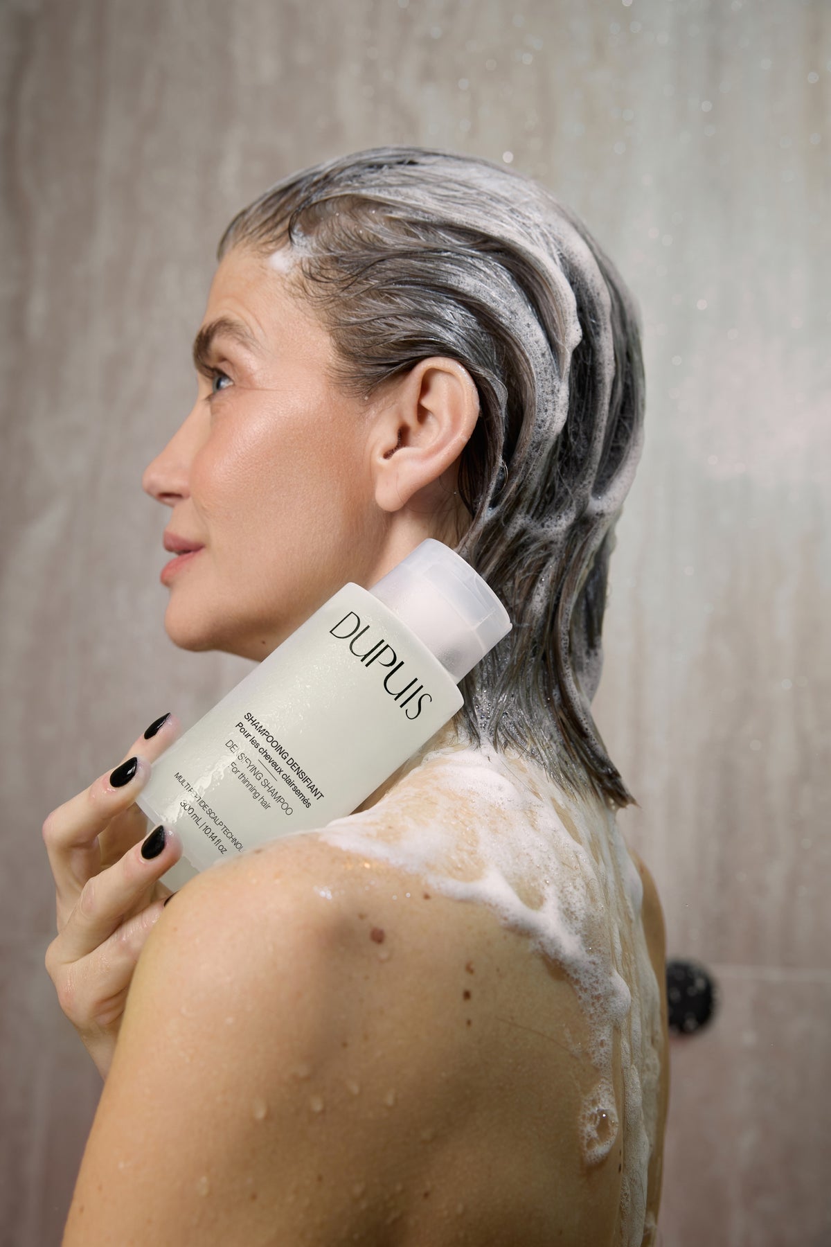 Femme faisant mousser le Shampooing Densifiant DUPUIS sur son cuir chevelu sous la douche
